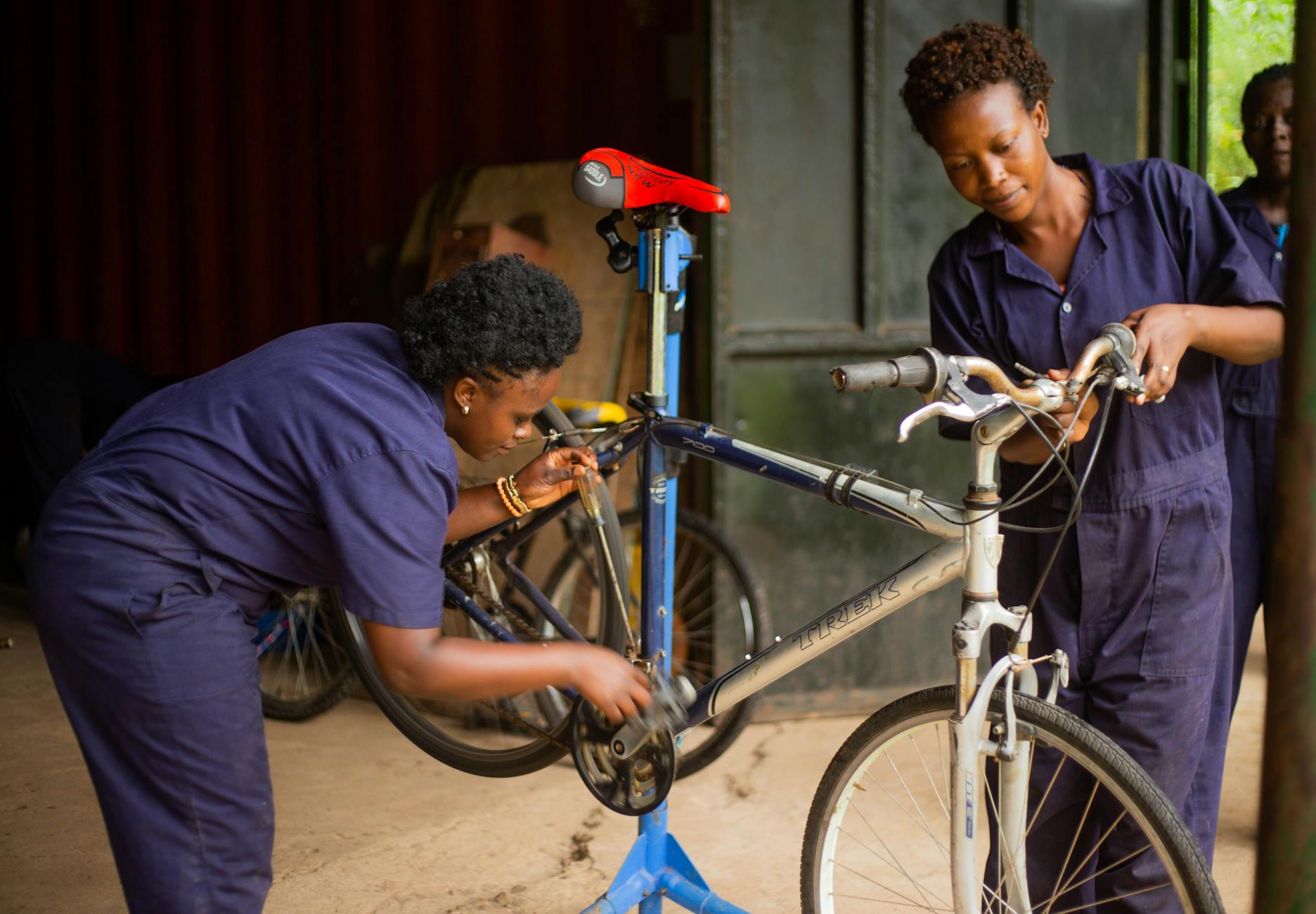 Dwie mechaniczki w niebieskich kombinezonach naprawiają rower w warsztacie