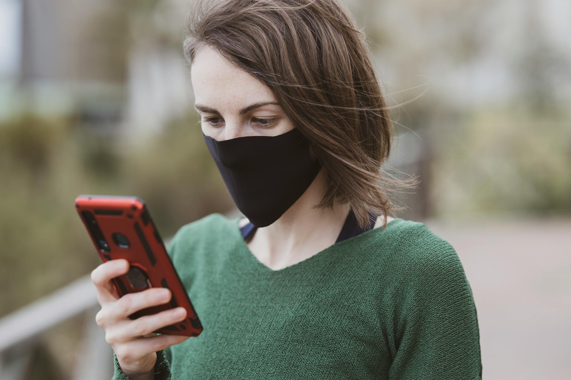 Kobieta w maseczce ochronnej przegląda smartfon na zewnątrz