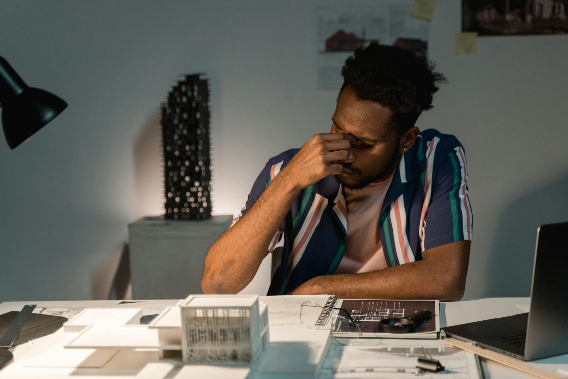 Zmęczony architekt nocą pracuje nad makietą i planami budynku